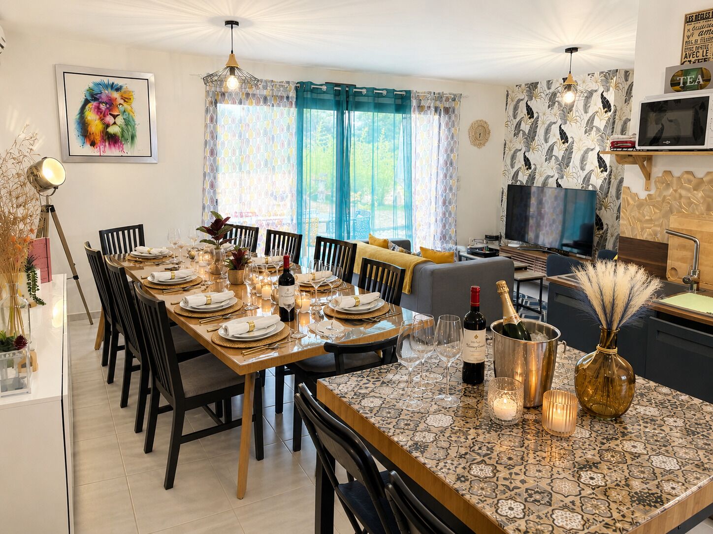 A dining area with a long table set for a meal, a television, and a kitchen area.