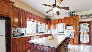 A kitchen with wooden cabinets, a central island, a ceiling fan, and a microwave. - Family Estate with High-Speed WiFi, Private Pool, Basketball, Office, & Patio (San Ignacio)