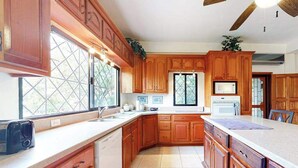 A kitchen with wooden cabinets, a dishwasher, a microwave, and a large window with a view. - Family Estate with High-Speed WiFi, Private Pool, Basketball, Office, & Patio (San Ignacio)