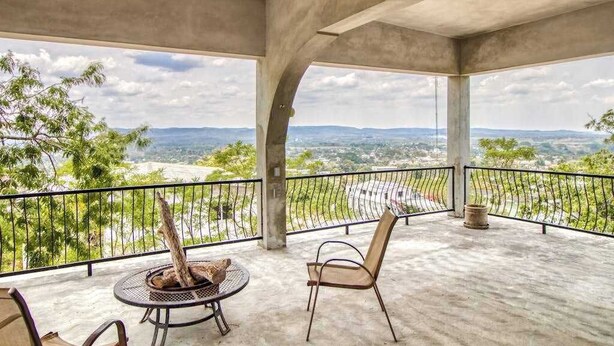 A covered outdoor area with a concrete floor, a metal table with chairs, and a view of distant hills. - Family Estate with High-Speed WiFi, Private Pool, Basketball, Office, & Patio (San Ignacio)