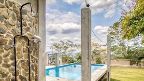 A stone wall with a metal shower, a concrete pool, and a view of trees and a fence. - Family Estate with High-Speed WiFi, Private Pool, Basketball, Office, & Patio (San Ignacio)