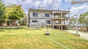 A two-story building with a balcony, a grassy yard, and a tree. - Family Estate with High-Speed WiFi, Private Pool, Basketball, Office, & Patio (San Ignacio)