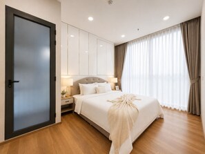 A modern hotel room with a large bed, a wardrobe, a nightstand with lamps, and a large window with curtains. - Centralworldbts (Bangkok)