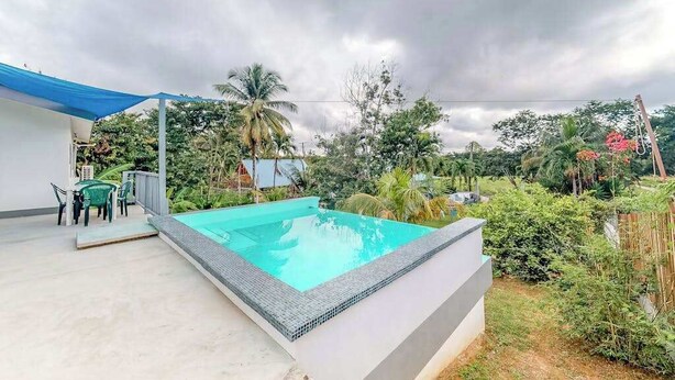 Une piscine recouverte d’une bâche bleue, entourée de verdure, sous un ciel nuageux.