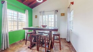 Un coin repas avec une table et des chaises en bois, de grandes fenêtres avec des rideaux et un mur vert.