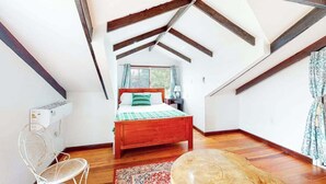 Ein Schlafzimmer im Dachgeschoss mit einem hölzernen Bett, einem Sessel, einem kleinen Tisch und einer Heizung.