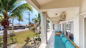 A covered outdoor seating area with a sofa and cushions, a palm tree, and a view of the street and buildings. - Spacious ground-floor condo with pool & patio - walk to ocean (San Pedro)