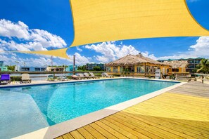 A swimming pool with a wooden deck, lounge chairs, and a thatched-roof building. - Apartment with WiFi, AC & shared outdoor pool - walk to the beach (San Pedro)