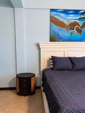 Ein Schlafzimmer mit einem Bett, einem runden Beistelltisch, einem Wandbild einer Meeresschildkröte und einem weißen Kopfteil.