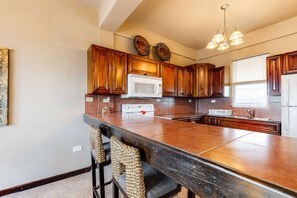 A kitchen with wooden cabinets, a white microwave, a stove, and a large island with bar stools. - Apartment with WiFi, AC & shared outdoor pool - walk to the beach (San Pedro)