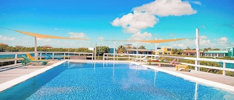 A rectangular swimming pool with a wooden deck, surrounded by lounge chairs and a white fence.