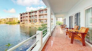 Ein Balkon mit Blick auf einen Fluss, Holzstühle und ein mehrgeschossiges Gebäude im Hintergrund.