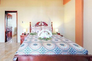 Una camera da letto con una coperta a motivi, una testata del letto in legno, lampade ai comodini e una porta che dà su un'altra stanza.
