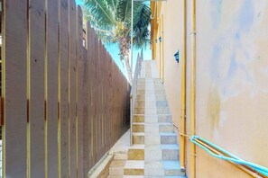 Un corridoio esterno stretto, con un recinto in legno da un lato e un muro giallo dall'altro, che conduce a una serie di gradini in pietra.