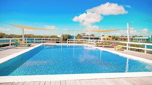En rektangulär pool med ett trädäck runt om, omgiven av ett vitt staket, och en klarblå himmel ovanför.
