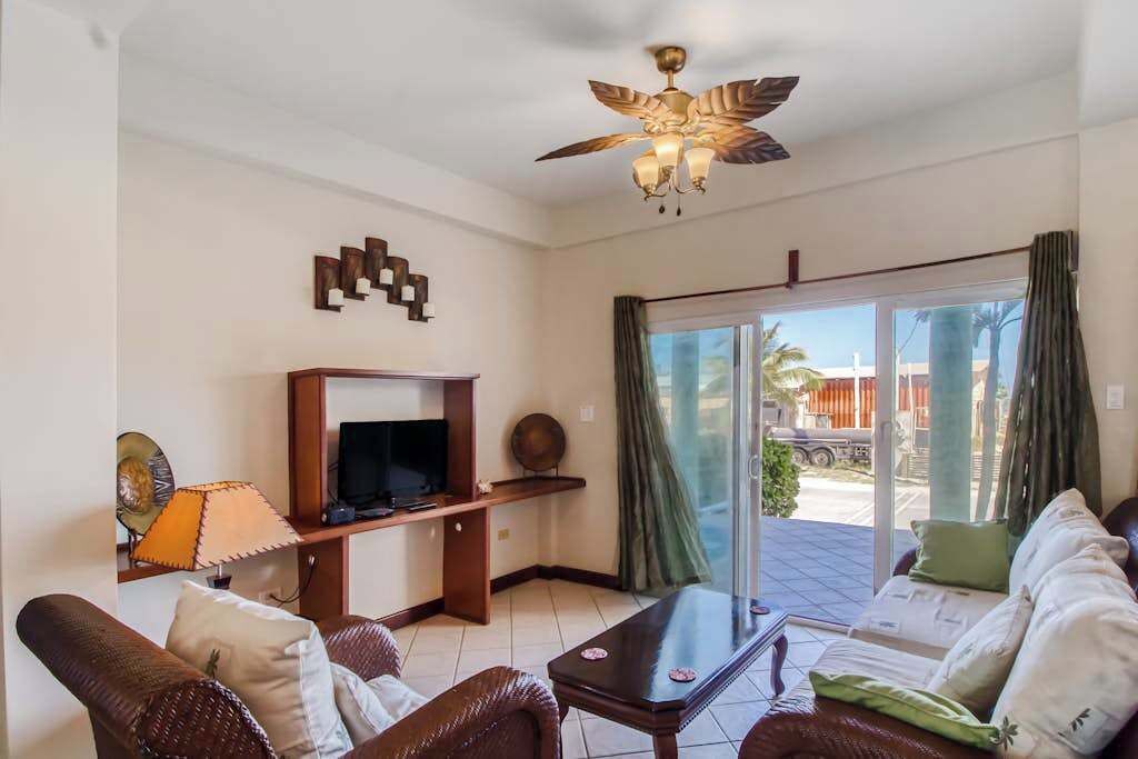 A living room with a TV, sofa, coffee table, ceiling fan, and a view through the glass door.
