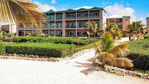 Een meerlaags hotel met een groen dak, omgeven door verzorgde tuinen en palmbomen.
