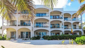 A multi-story hotel with balconies, a sandy courtyard, and palm trees. - Relaxing condo with shared pool, ocean views, partial AC & WiFi (San Pedro)
