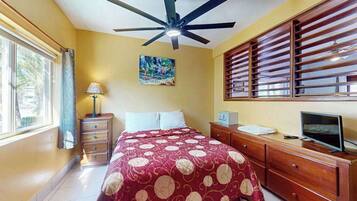 A bedroom with a bed, a ceiling fan, a window with blinds, a desk with a computer, and a TV.