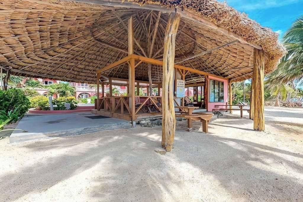 Een rieten dakconstructie met houten frame, een bank en een bord dat een resort aangeeft.