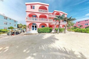 Un hotel rosa de varios pisos con balcones, un estacionamiento y palmeras.