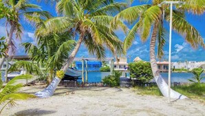 Una playa con palmeras, un bote y edificios al fondo.