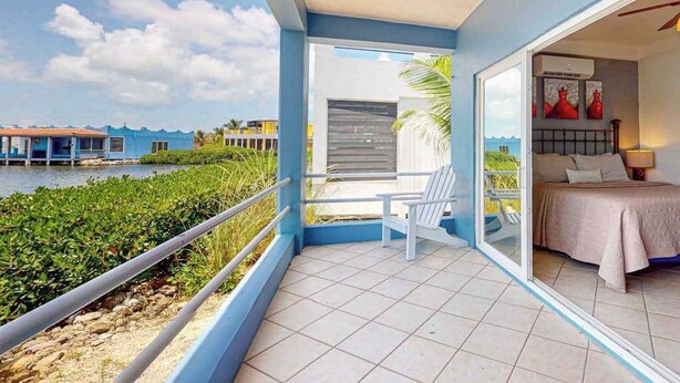 A balcony with a view of the water, a bed with a view, and a ceiling fan. - Waterfront villa with outdoor pool, washer dryer, & central AC (San Pedro)