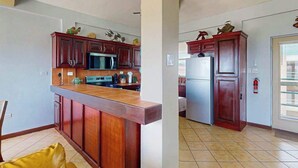 A kitchen with wooden cabinets, a microwave, a refrigerator, and a tiled floor. - Steps from the sea apartment with shared pool & ocean-view balcony (San Pedro)