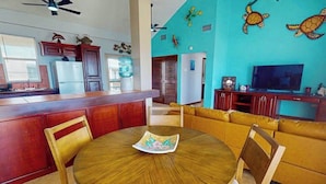 A living room with a round wooden table, yellow sofa, and a TV. - Steps from the sea apartment with shared pool & ocean-view balcony (San Pedro)