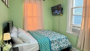 Un dormitorio con cama, mesita de noche, lámpara, televisor y ventana.