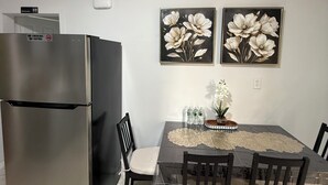 Un comedor con una mesa, sillas, un refrigerador y dos cuadros de flores colgados en la pared.