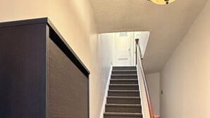 Una escalera con peldaños alfombrados, barandilla de madera y una puerta cerrada en la parte superior.