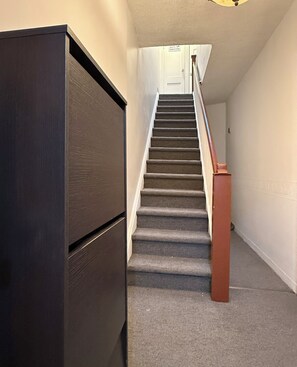 Una escalera con peldaños alfombrados, barandilla de madera y una puerta cerrada en la parte superior.