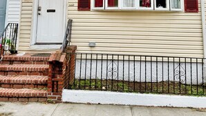 Una casa de dos pisos con puerta principal, un porche pequeño y una escalera de ladrillo.