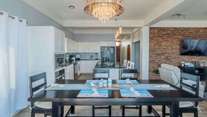 A modern kitchen with white cabinets, a central island, and a dining area with a dark table set for six. - Amazing 2 story oceanfront house with pool, balcony, central AC, & WD (San Pedro)