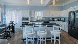 A modern kitchen with white cabinets, a central island with bar stools, a refrigerator, and pendant lighting. - Amazing 2 story oceanfront house with pool, balcony, central AC, & WD (San Pedro)