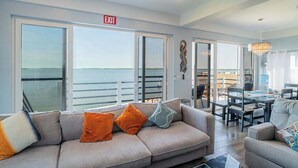 A modern living room with a sofa, a dining area, and large windows with an ocean view. - Amazing 2 story oceanfront house with pool, balcony, central AC, & WD (San Pedro)