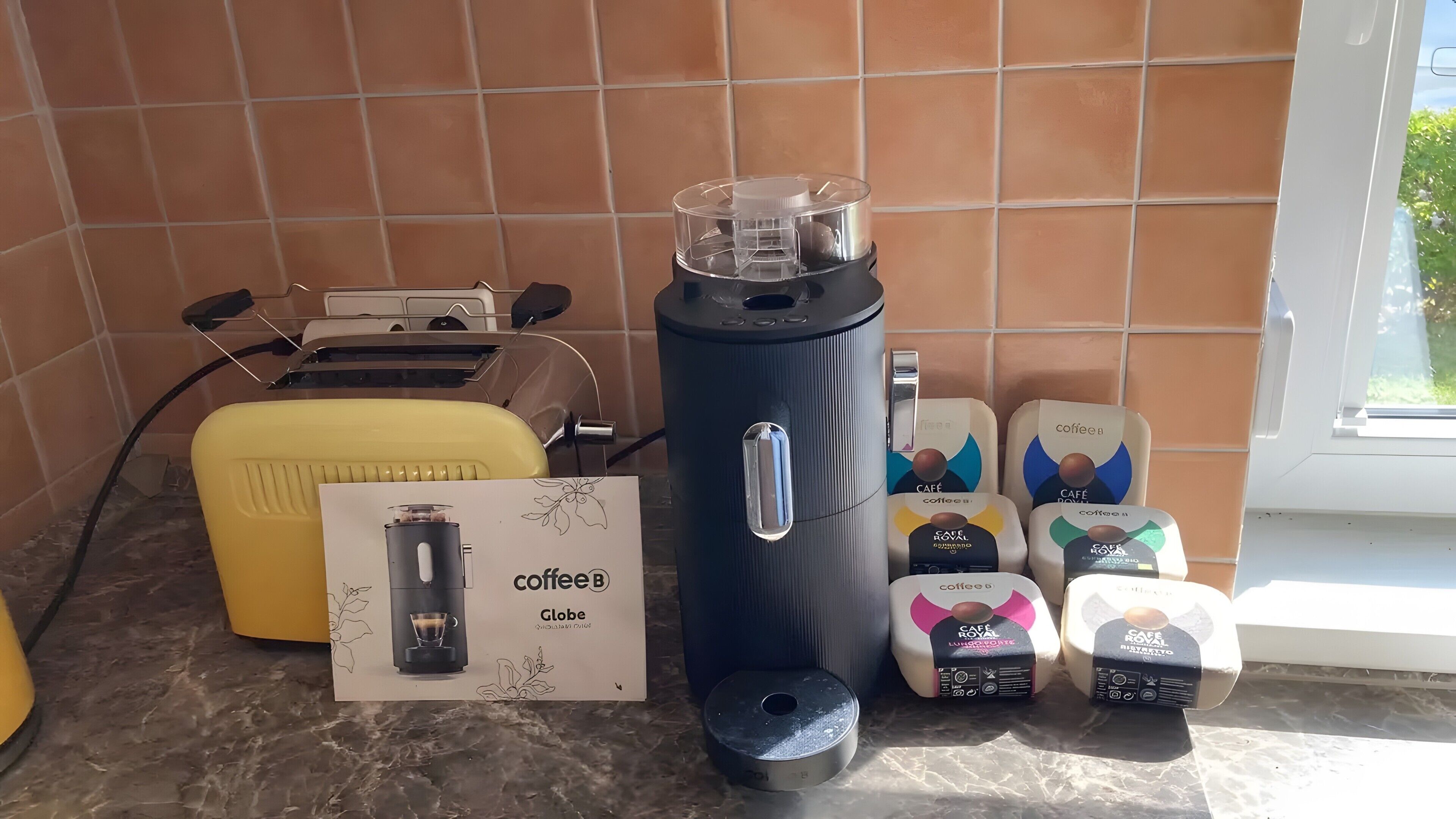 A coffee maker, a toaster, and coffee pods on a kitchen counter.