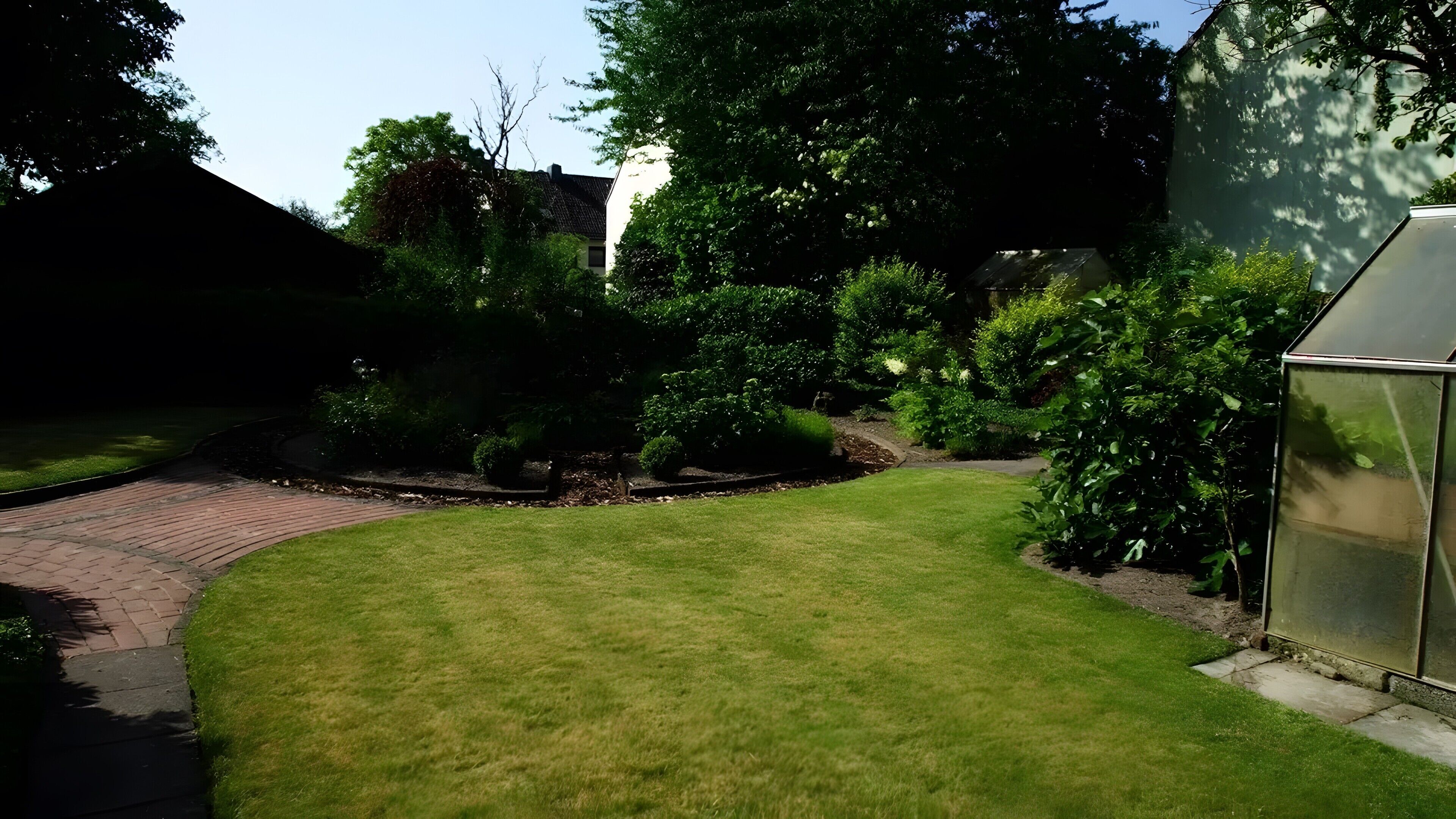 A well-maintained lawn, a brick pathway, and a greenhouse structure.