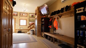 Una habitación con piso de madera, un televisor montado en la pared, un estante con sombreros y una ventana con luz natural.