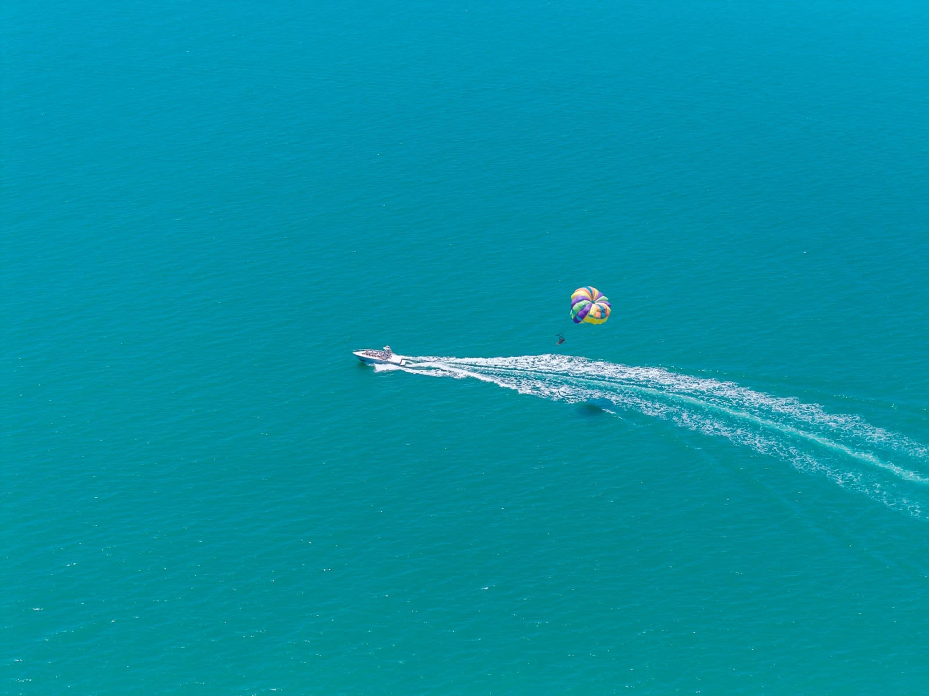 An aerial view of a boat creating a wake in turquoise water.