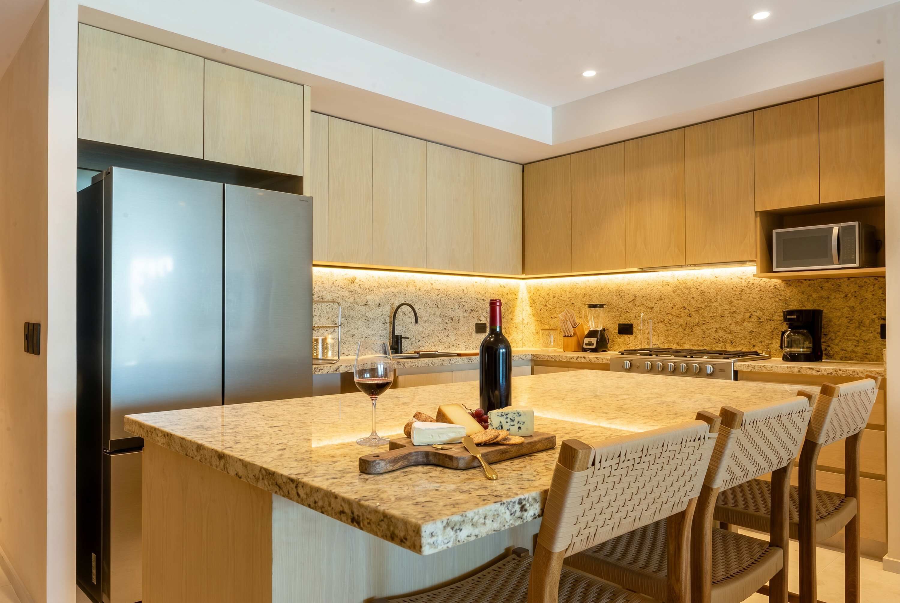 Eine moderne Küche mit Kochinsel, Edelstahlkühlschrank, Holzschränken und einer Arbeitsplatte aus Granit, sowie einem Weinglas.