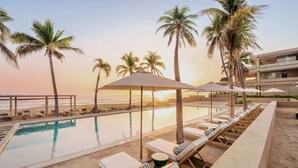 A pool area with lounge chairs and umbrellas, palm trees, and a view of the ocean. - Anera | Private Oceanfront Garden (Playa Blanca)