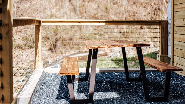 Un banco de madera con patas de metal en un espacio al aire libre con suelo de grava.