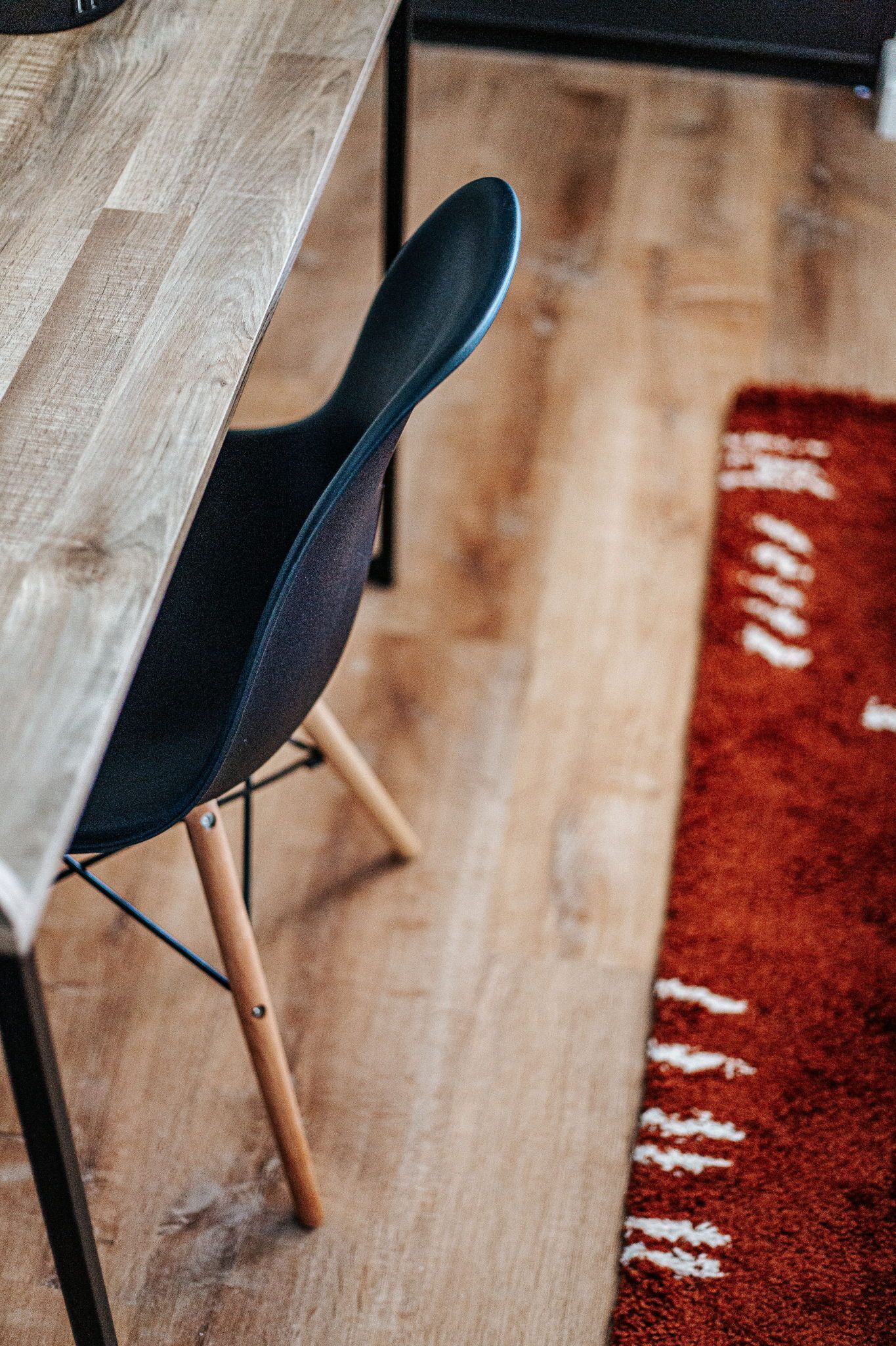 Une table en bois, une chaise noire, un tapis rouge et un plancher en bois.