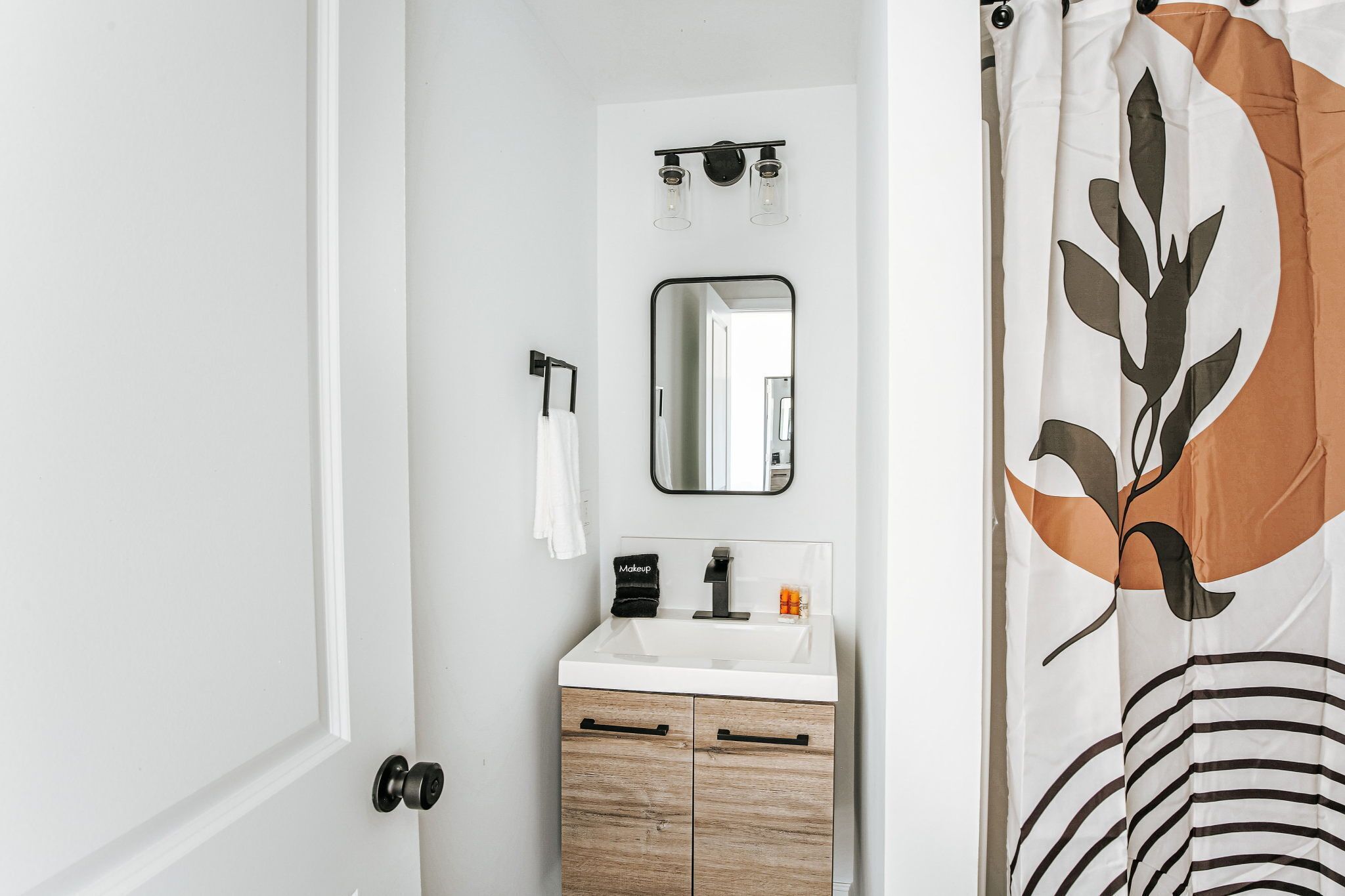 A bathroom with a white sink, a mirror, a towel rack, and a shower curtain with a leaf design.