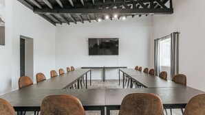 Un salón de conferencias con una larga mesa, sillas, un cuadro en la pared y una ventana con cortinas.