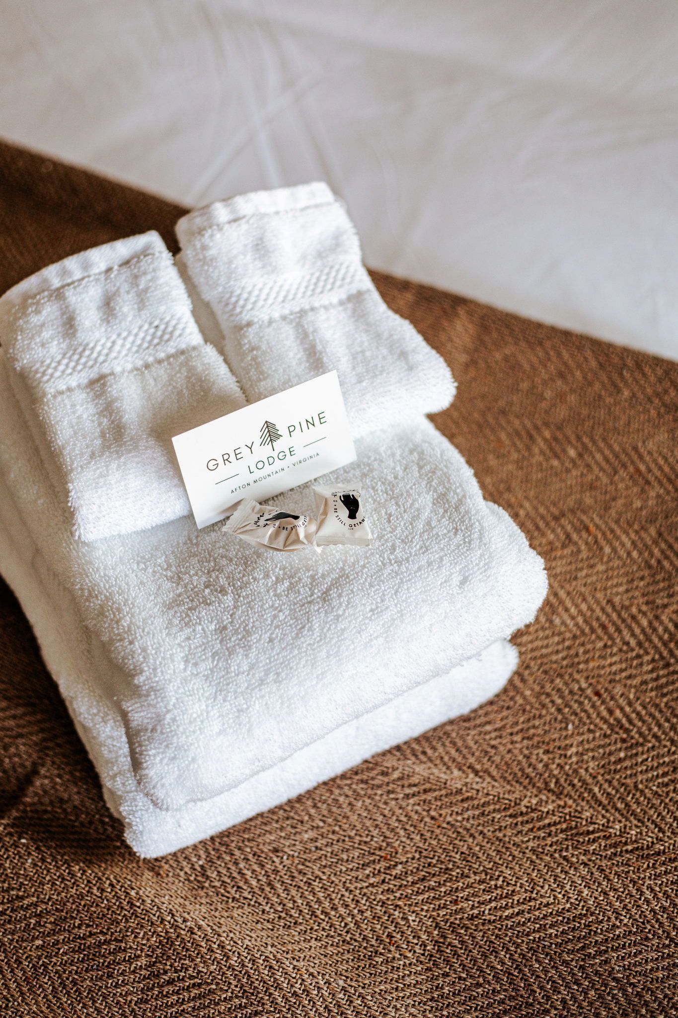 A neatly folded white towel with a tag labeled 'Grey Pine Lodge' on a textured brown surface.