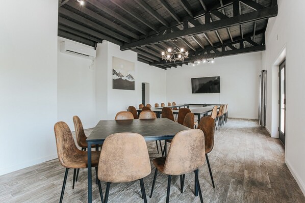 A conference room with a long table, multiple chairs, a chandelier, and a mounted TV.