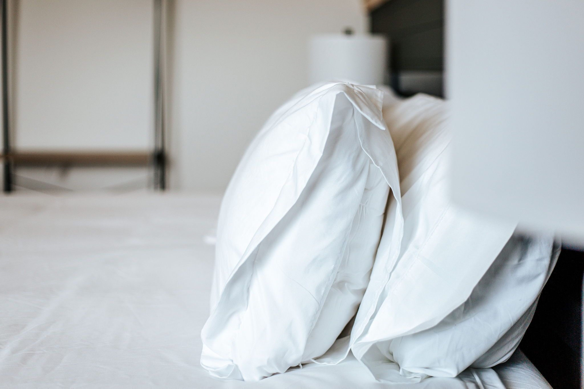 A bed with white bedding in a room with a plain wall and a visible door frame.